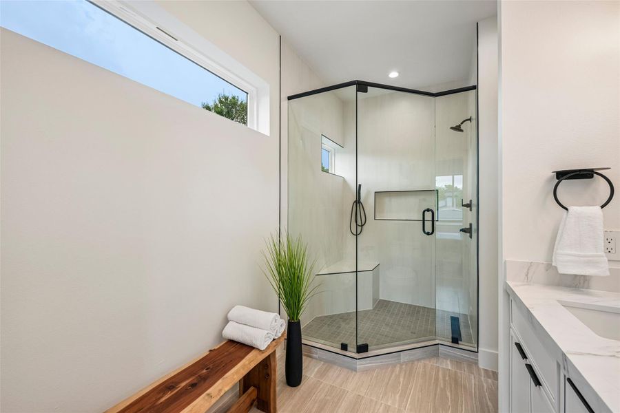A glass-enclosed shower, a long transom window, and a sleek vanity create a serene bathroom oasis.