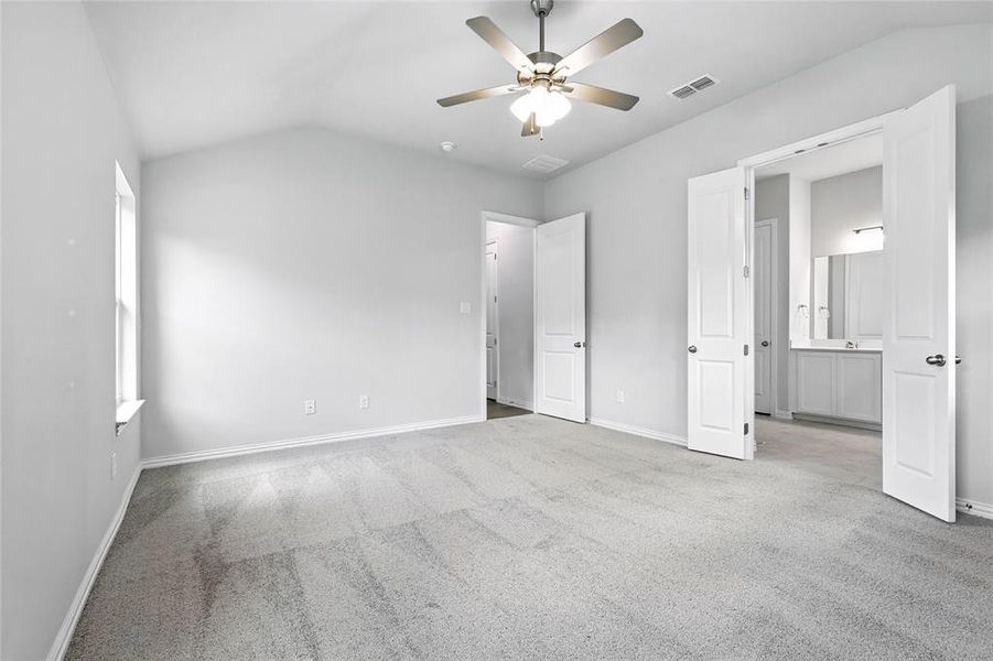 Unfurnished bedroom featuring vaulted ceiling, light carpet, a ceiling fan, and ensuite bathroom