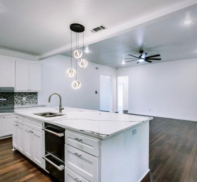 Kitchen featuring light stone countertops, ceiling fan, a center island with sink, decorative light fixtures, and dark hardwood / wood-style flooring