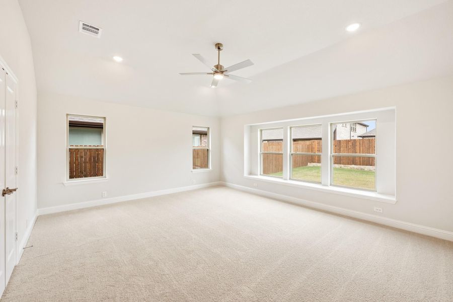 Empty bedroom with carpet flooring, ceiling fan, and large windows overlooking a fenced backyard