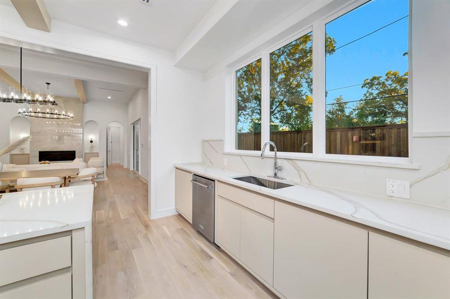 Kitchen featuring light stone counters, light wood-style floors, beam ceiling, modern cabinets, and a premium fireplace Kitchen featuring light stone counters, light wood-style floors, beam ceiling, modern cabinets, and a premium fireplace