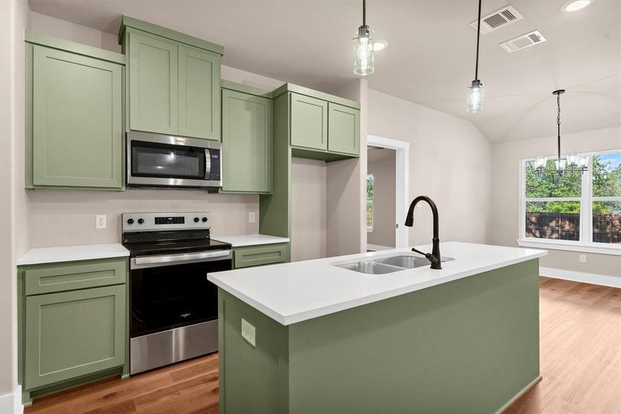 Kitchen featuring green cabinetry, appliances with stainless steel finishes, decorative light fixtures, light wood-type flooring, and vaulted ceiling Kitchen featuring green cabinetry, appliances with stainless steel finishes, decorative light fixtures, light wood-type flooring, and vaulted ceiling