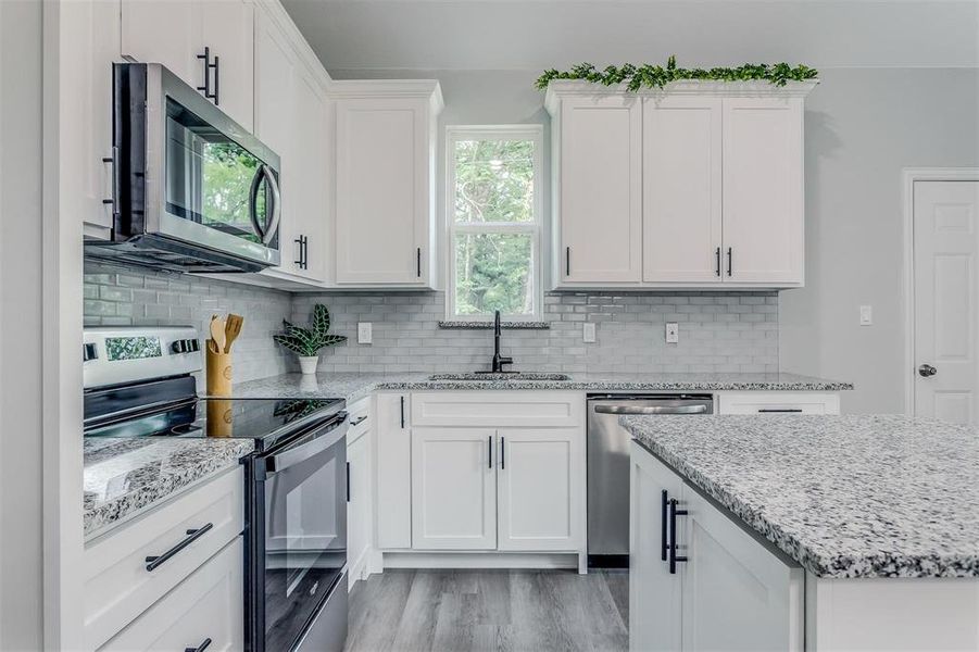 Kitchen with white cabinets, sink, decorative backsplash, light hardwood / wood-style floors, and stainless steel appliances