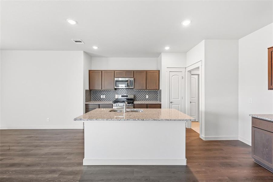 Kitchen with light stone countertops, a center island with sink, appliances with stainless steel finishes, dark wood-type flooring, and recessed lighting Kitchen with light stone countertops, a center island with sink, appliances with stainless steel finishes, dark wood-type flooring, and recessed lighting