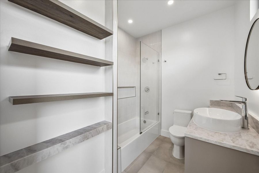 Modern bathroom featuring a glass-enclosed shower-tub combo, elegant vessel sink, and stylish open shelving for a contemporary touch. Modern bathroom featuring a glass-enclosed shower-tub combo, elegant vessel sink, and stylish open shelving for a contemporary touch.