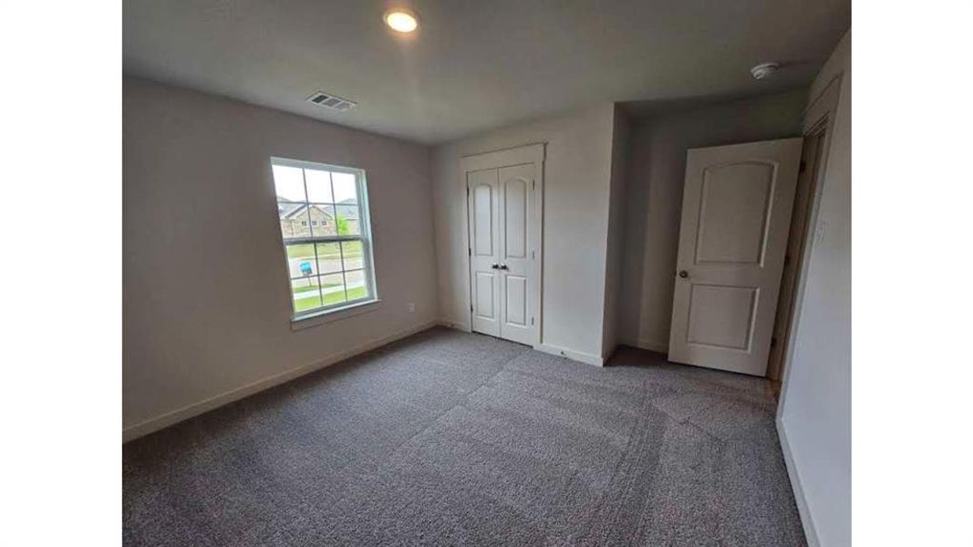 Spacious room featuring neutral paint, gray carpeting, a multi-pane window, and a double-door closet Spacious room featuring neutral paint, gray carpeting, a multi-pane window, and a double-door closet