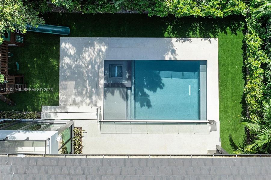 Modern residence featuring a clean-lined architectural facade with expansive glass panels, rendered white exterior walls, and manicured green lawn bordered by mature landscaping