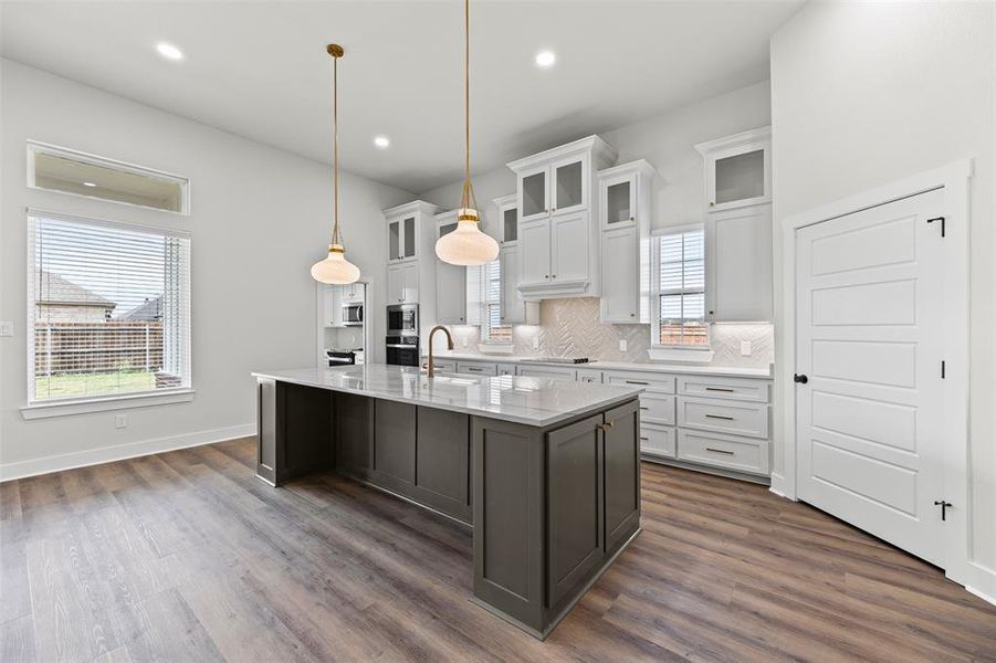 Kitchen featuring white cabinetry, glass insert cabinets, tasteful backsplash, an island with sink, and recessed lighting Kitchen featuring white cabinetry, glass insert cabinets, tasteful backsplash, an island with sink, and recessed lighting