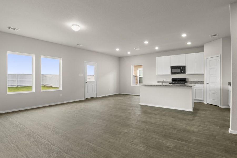Image of living room with dark wood-like flooring and light grey painted walls with a kitchen in the distance