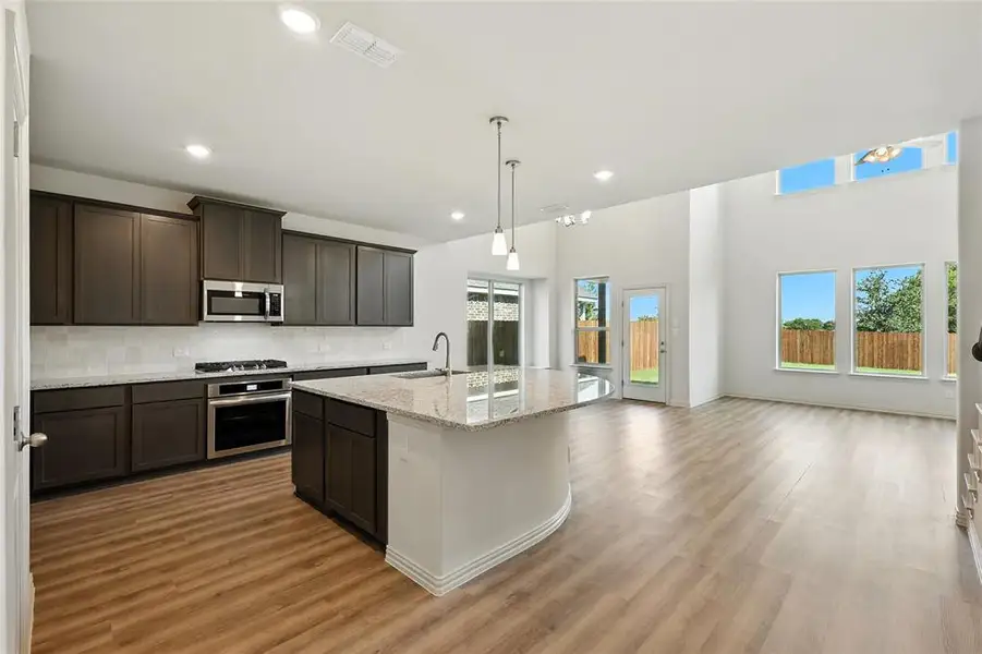 Kitchen featuring light stone countertops, decorative backsplash, dark wood finish cabinets, stainless steel appliances, and a high ceiling Kitchen featuring light stone countertops, decorative backsplash, dark wood finish cabinets, stainless steel appliances, and a high ceiling