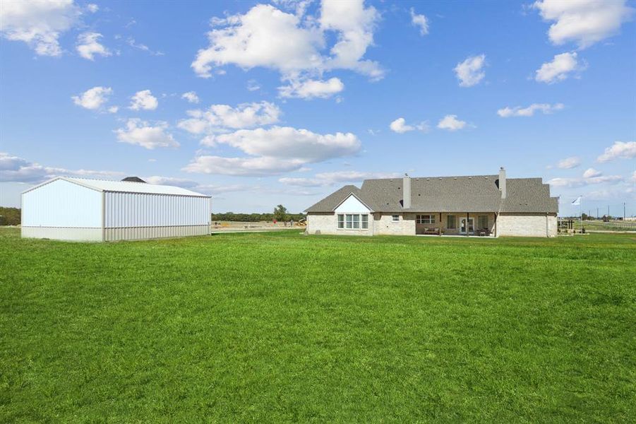 Expansive green lawn featuring a large metal outbuilding and a brick exterior home with a covered patio