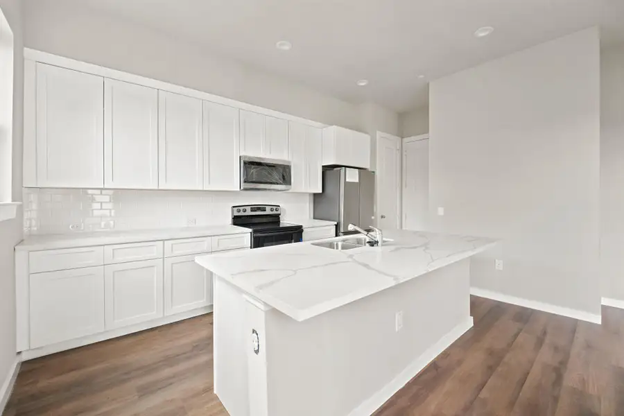 White shaker cabinets, sleek stone countertops, and warm wood-style flooring anchor this modern kitchen space.