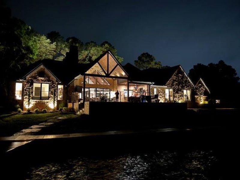 Back of house at twilight with stone siding, a patio, a chimney, and a lawn