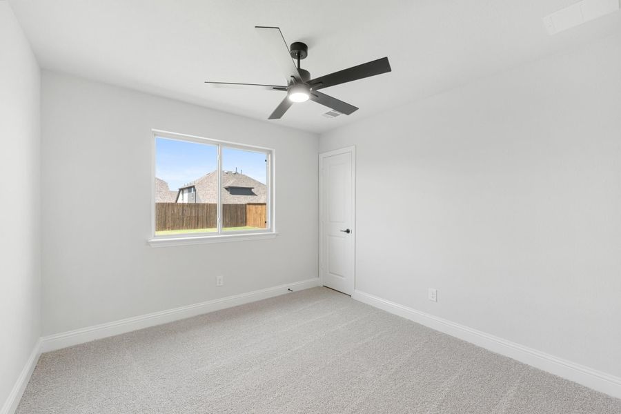 Empty bedroom with gray carpet, white walls, ceiling fan, and single window with backyard view Empty bedroom with gray carpet, white walls, ceiling fan, and single window with backyard view