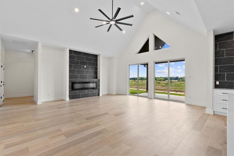 living room featuring a fireplace, high vaulted ceiling, lighting, and light wood finished floors living room featuring a fireplace, high vaulted ceiling, lighting, and light wood finished floors