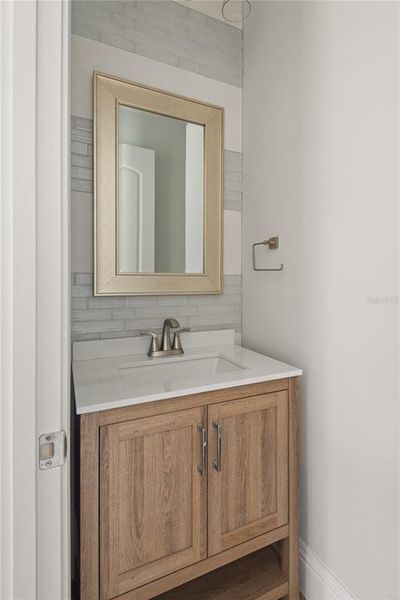 Conveniently located near the kitchen and lanai, this powder bath features a stylish vanity with a light wood finish, a white countertop, and a decorative mirror.