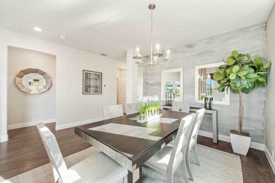 Dining room with dark wood table, white chairs, chandelier, and accent wall with hardwood floors