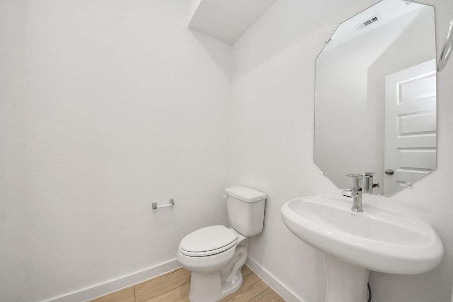 This half bathroom features a stylish pedestal sink, modern hardware, and bright recessed lighting, creating a sleek and inviting space. Sample photo of completed home with similar floor plan. Actual colors and selections may vary.