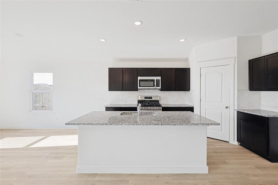 Kitchen featuring light stone countertops, appliances with stainless steel finishes, light hardwood / wood-style flooring, and a kitchen island with sink