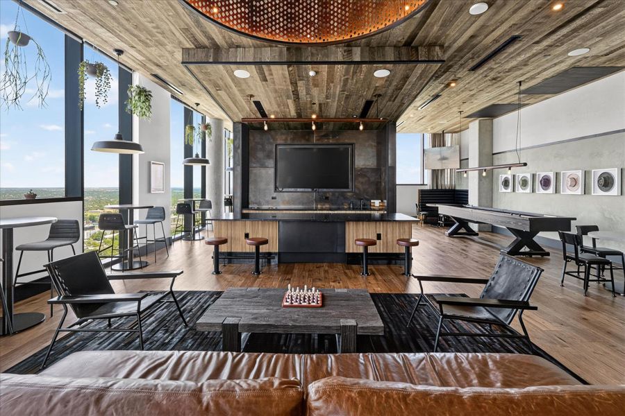 City views and natural light illuminate a spacious game room with rich wood flooring and a modern bar.