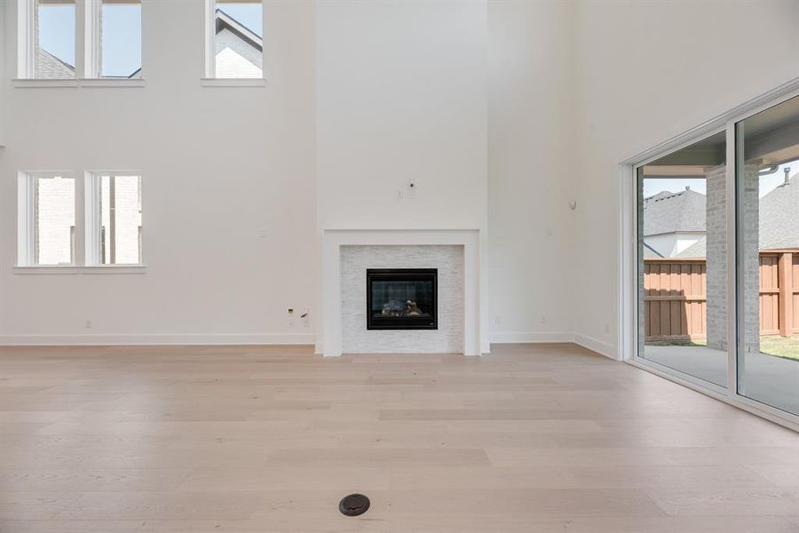 Unfurnished living room with a high ceiling, light wood-style flooring, and a glass covered fireplace
