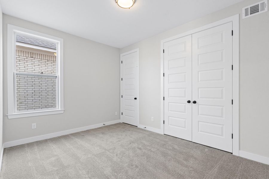 Light gray wall paint, gray carpet, white trim, white paneled doors with matte black hardware, and an overhead flush mount light fixture Light gray wall paint, gray carpet, white trim, white paneled doors with matte black hardware, and an overhead flush mount light fixture