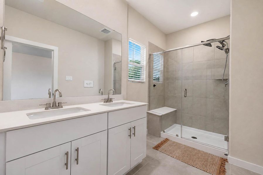Primary bathroom features a long dual-sink vanity, expansive wall mirror, modern fixtures, and a large tiled walk-in shower with glass enclosure. A window brings in natural light, while the neutral tile, white cabinetry, and clean contemporary finishes create a bright and polished everyday retreat. Primary bathroom features a long dual-sink vanity, expansive wall mirror, modern fixtures, and a large tiled walk-in shower with glass enclosure. A window brings in natural light, while the neutral tile, white cabinetry, and clean contemporary finishes create a bright and polished everyday retreat.