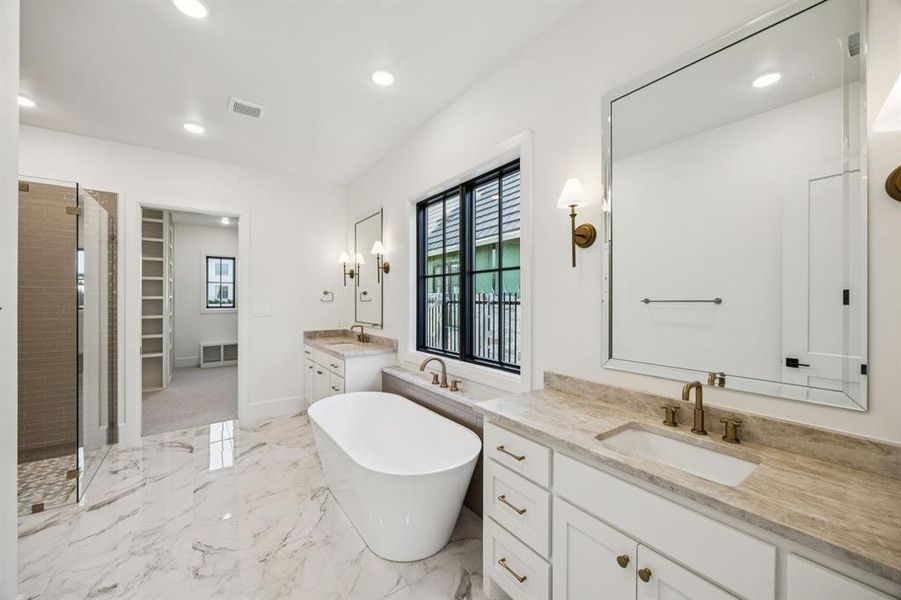 Bathroom featuring two vanities, a stall shower, a freestanding tub, marble tiled flooring, and a walk in closet Bathroom featuring two vanities, a stall shower, a freestanding tub, marble tiled flooring, and a walk in closet