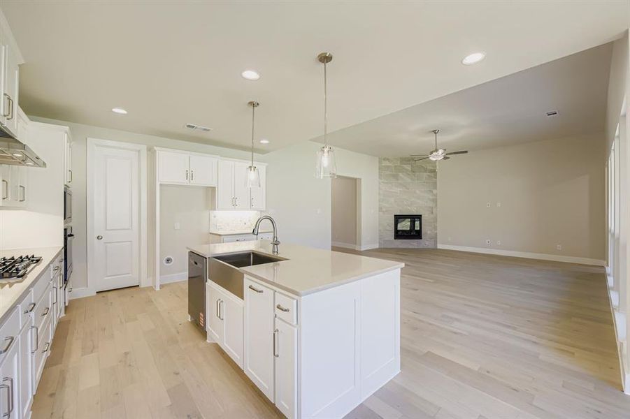 Kitchen with white cabinets, hanging light fixtures, a kitchen island with sink, light wood-style floors, and recessed lighting