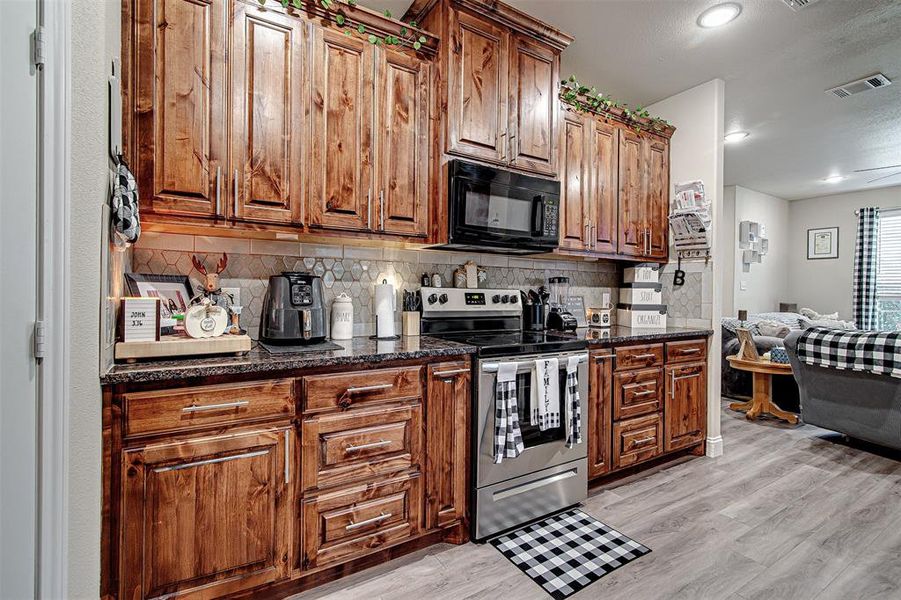 Kitchen with backsplash, dark stone counters, stainless steel range with electric cooktop, and light hardwood / wood-style floors