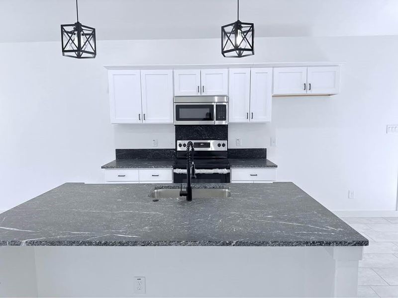 Kitchen featuring white cabinetry, dark stone counters, stainless steel appliances, and hanging light fixtures Kitchen featuring white cabinetry, dark stone counters, stainless steel appliances, and hanging light fixtures