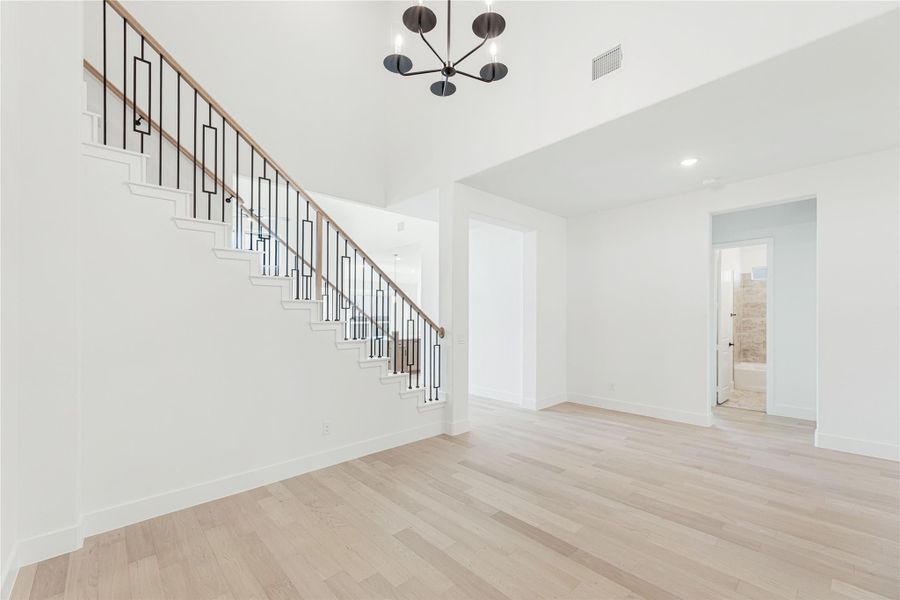Open foyer with staircase, black iron balusters, light hardwood floors, and modern chandelier