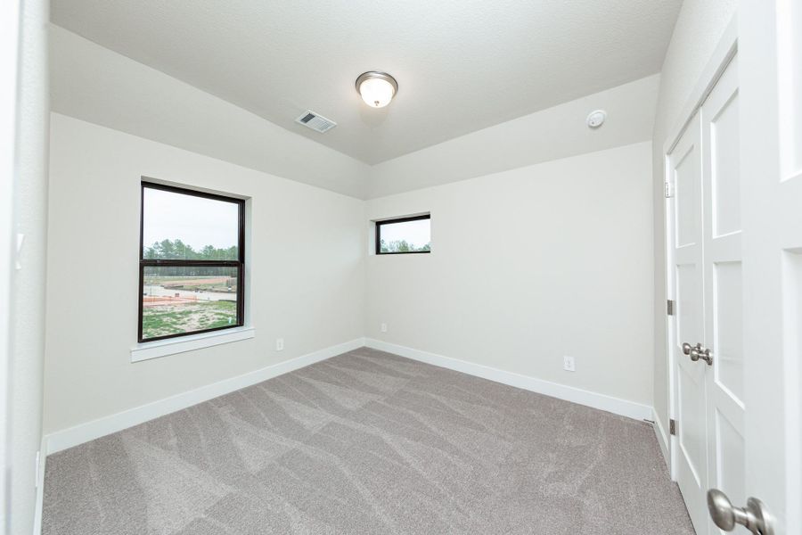 This secondary bedroom features high ceilings, plush carpet, and windows to brighten up this space with natural lighting.