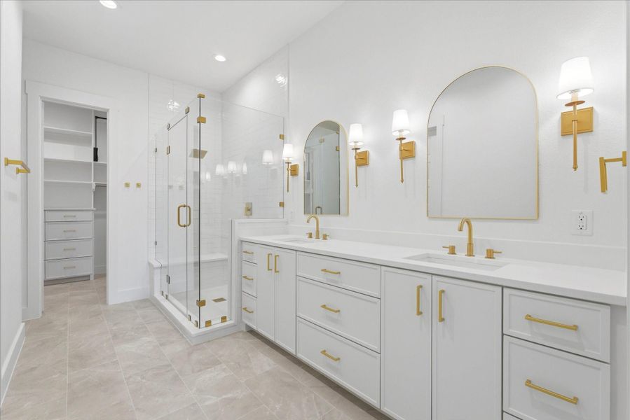 The stunning primary bathroom features stylish gold hardware and finishes, decorative mirrors, elegant wall sconces, and plenty of storage for a polished, functional feel.