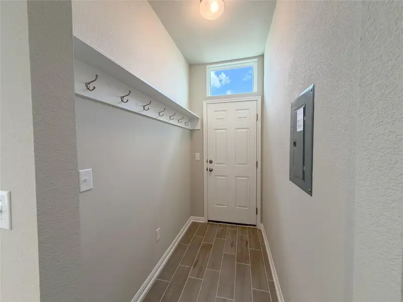 Entryway featuring wood-finish tile flooring, a white paneled door with an upper transom window, built-in coat hooks with an overhead shelf, and a ceiling-mounted light fixture