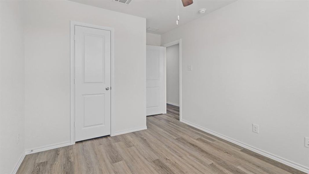Spacious room featuring wood-finish flooring, white baseboards, and white painted walls Spacious room featuring wood-finish flooring, white baseboards, and white painted walls