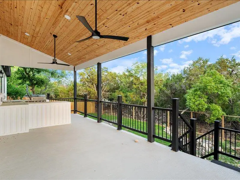 Expansive outdoor living space featuring a wood plank ceiling, two ceiling fans, and a built-in outdoor kitchen with a sink