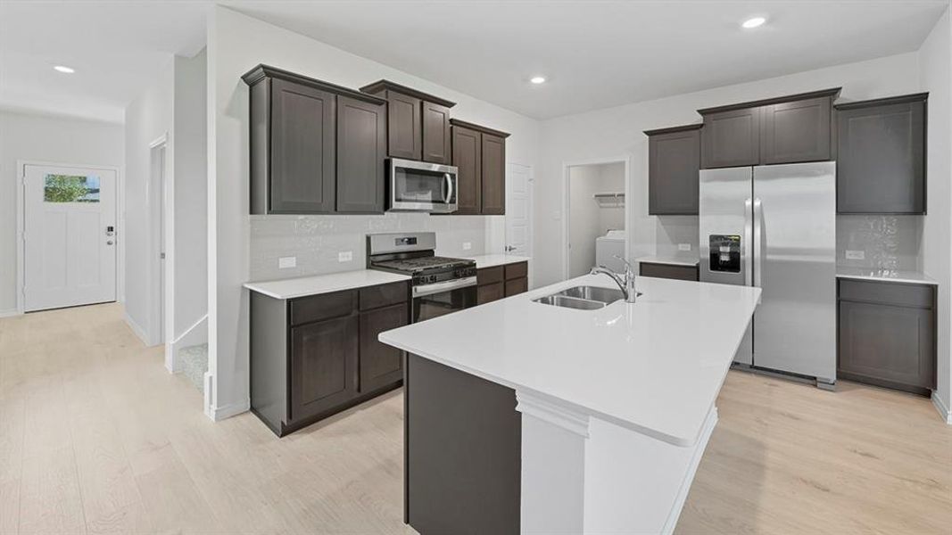 Kitchen featuring appliances with stainless steel finishes, decorative backsplash, an island with sink, light wood-style flooring, and recessed lighting