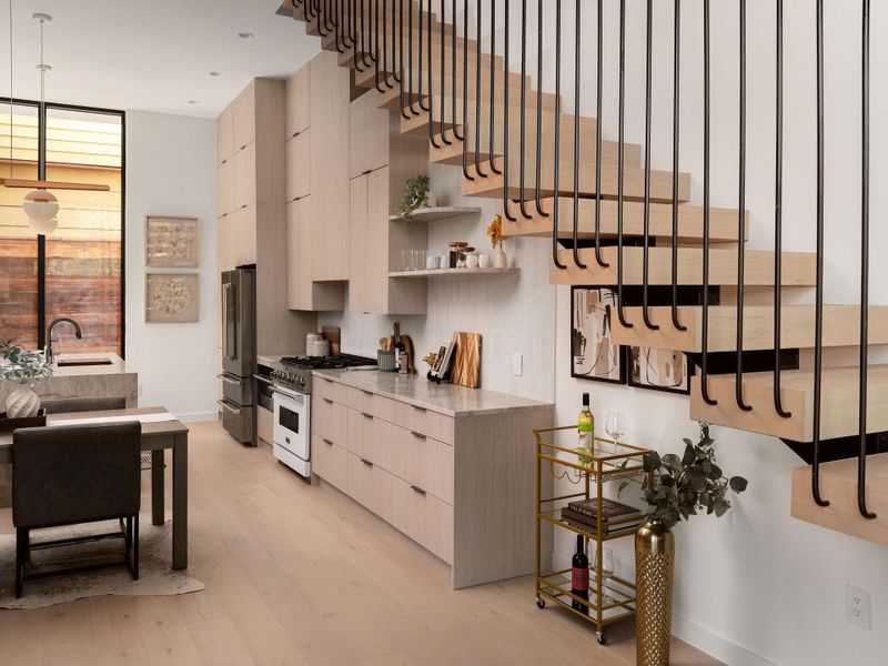 Minimalist cabinetry and custom stone countertops anchor this modern kitchen beneath a floating wood staircase.
