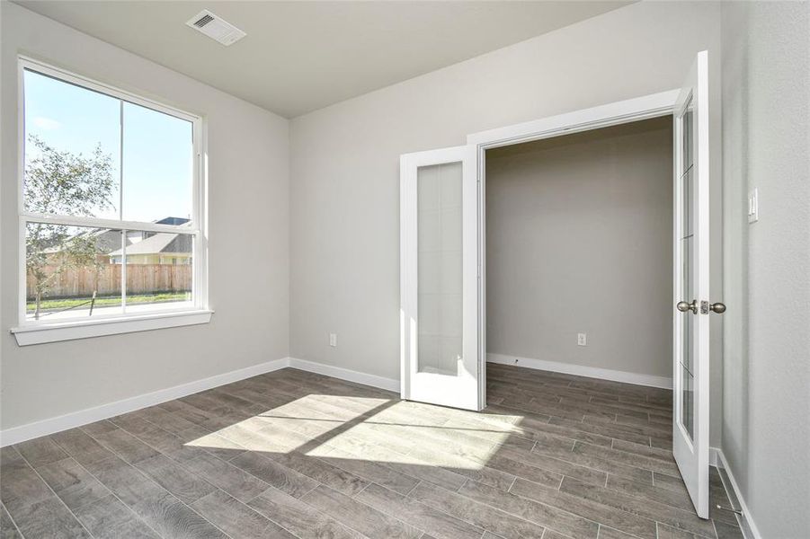 At the forefront, a refined home office beckons productivity and focus. Luxurious details like wood-look tile flooring, custom paint, expansive windows with privacy blinds, and French doors create an inspiring workspace. Sample photo of completed home with similar floor plan. Actual colors and selections may vary.