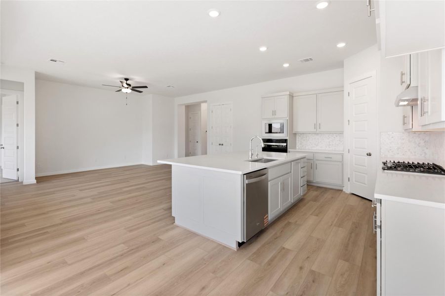 Kitchen featuring light wood-style floors, a kitchen island with sink, white cabinets, tasteful backsplash, and recessed lighting
