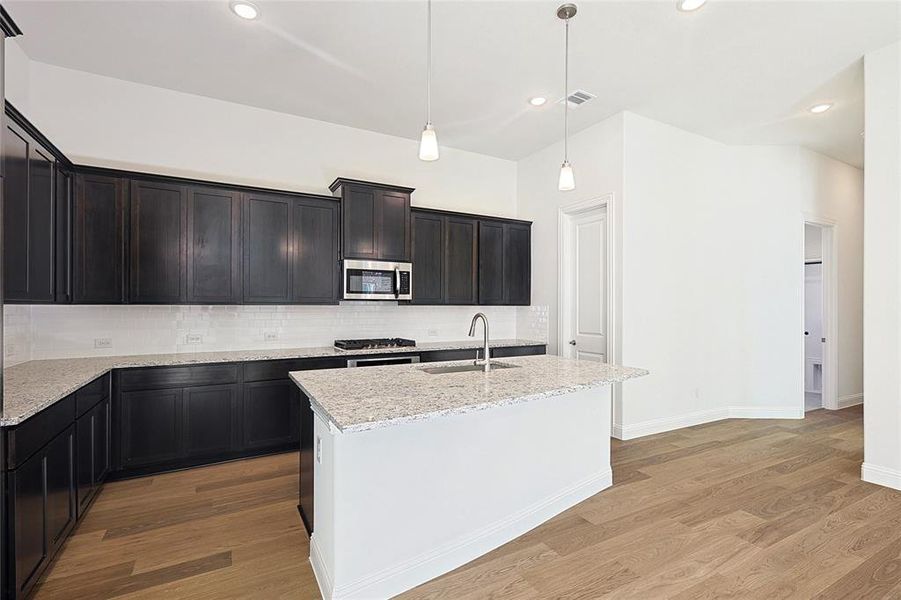 Kitchen with tasteful backsplash, stainless steel appliances, a kitchen island with sink, decorative light fixtures, and light hardwood / wood-style floors