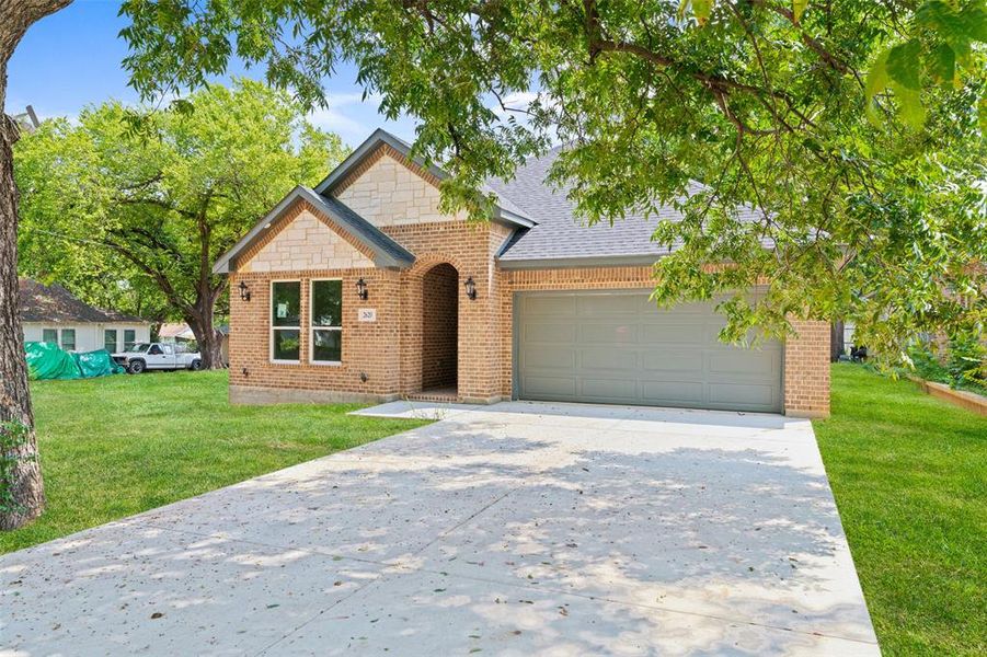 View of front of house with brick siding, an attached garage, a front lawn, and concrete driveway