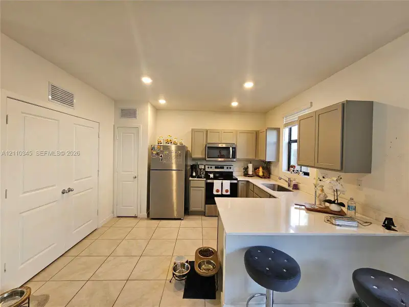 Kitchen featuring stainless steel appliances, quartz countertops, neutral cabinetry, recessed lighting, and tile flooring