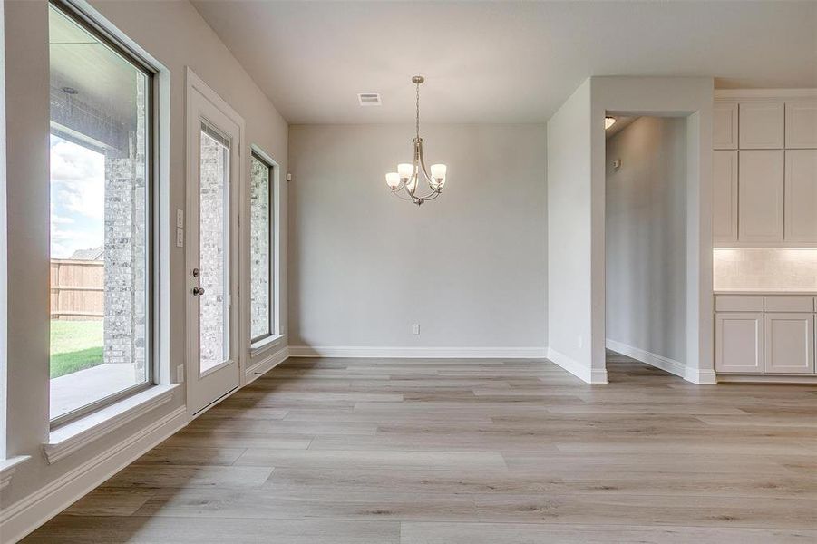 Unfurnished dining area with a notable chandelier, a wealth of natural light, and light wood-type flooring