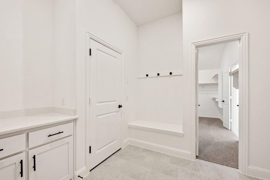 Mudroom with built-in bench, wall hooks, white cabinets, and tile floor leading to carpeted closet area