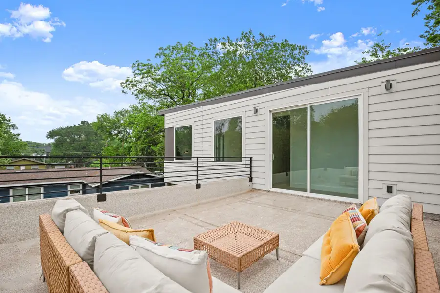 Spacious rooftop deck featuring a textured concrete surface, horizontal metal railing, and a sliding glass door providing access to the interior
