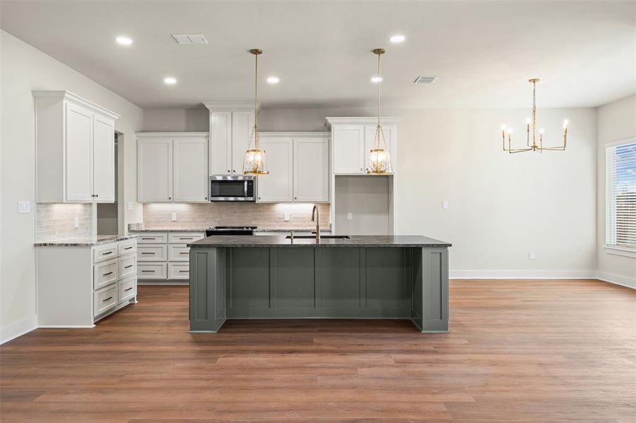 Kitchen with white cabinets, a center island with sink, a chandelier, a kitchen breakfast bar, and hanging light fixtures