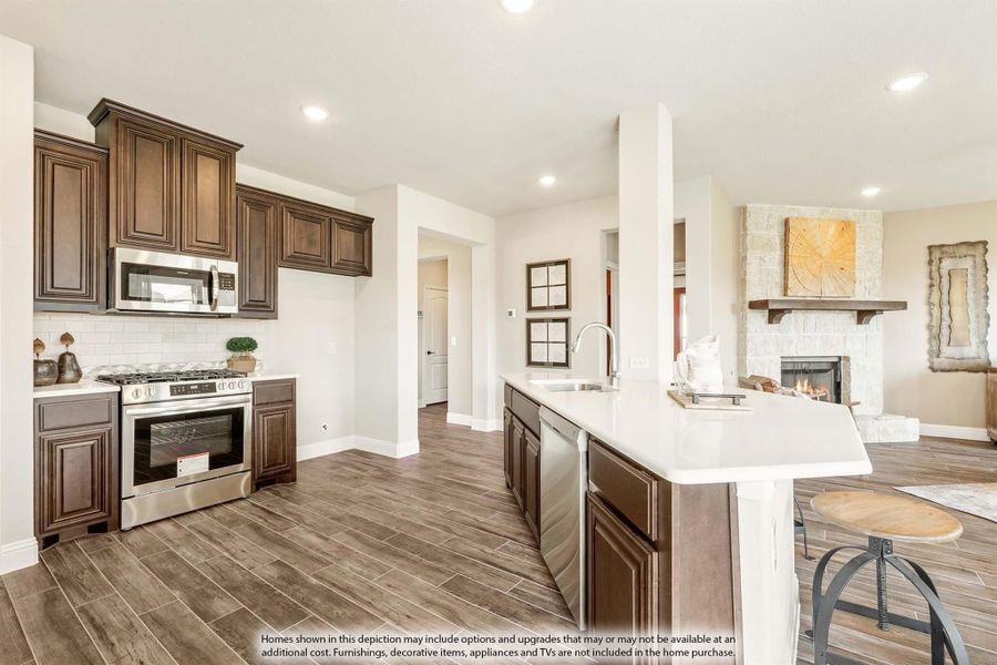 Kitchen with dark wood cabinets, white island, stainless steel appliances, and wood-look tile floors open to living room with fireplace. Kitchen with dark wood cabinets, white island, stainless steel appliances, and wood-look tile floors open to living room with fireplace.