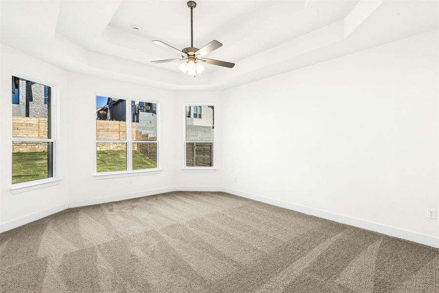 Carpeted empty room with a raised ceiling and a ceiling fan